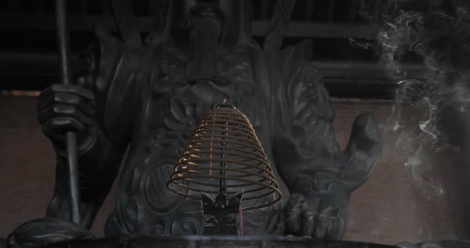 Tilt shot of burning circular incense and bronze statue of warrior in Bai Dinh Temple, Vietnam