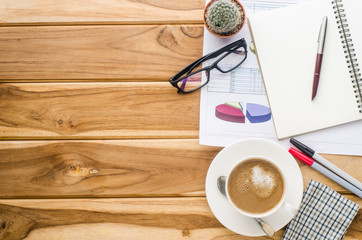 coffee cup, chart, pen, notebook and accessory for work on wooden table.