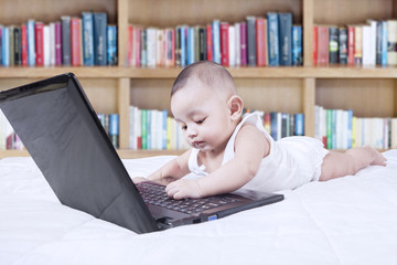 Funny toddler with laptop and bookcase