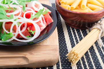 Black plate with fresh salad of tomatoes, onions and arugula