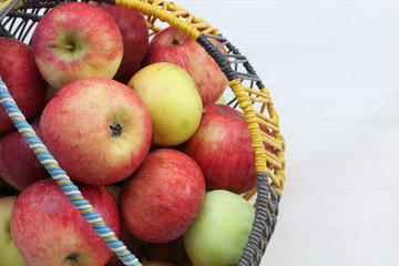 harvest fresh fruit/ many apples in a rustic wicker basket on a light wooden background 