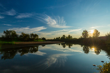 Mirror reflection of blue sky, clouds and sunset colors in wild river, in spring