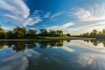 Mirror reflection of blue sky, clouds and sunset colors in wild river, in spring