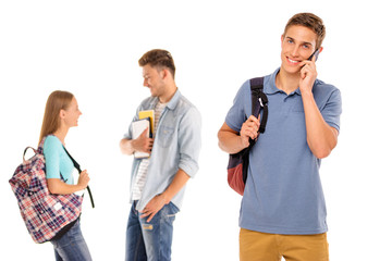 Enjoying student life. Handsome young man talking on the mobile phone and smiling with his friends chatting in the background. Isolated on white.