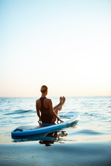 Silhouette of beautiful girl practicing yoga on surfboard at sunrise.