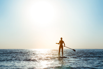 Silhouette of young beautiful girl surfing in sea at sunrise.