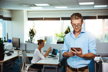Young successful businessman smiling, looking at tablet, over office background.