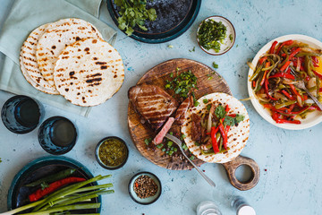 Mexican combo and flank steak, colorful pepper fajitas on flatbread over grey tabletop.