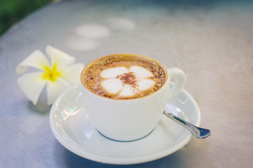 A cup of coffee plumeria pattern in a white cup on wooden background