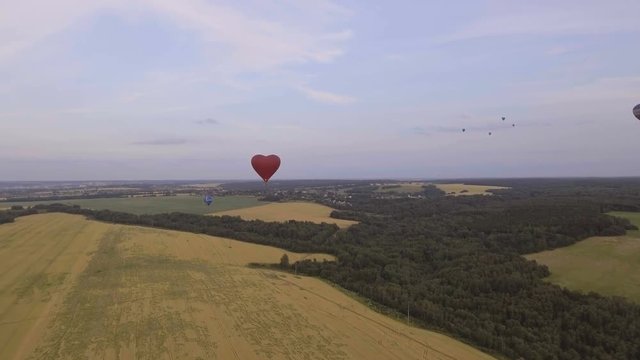 Red balloon in the shape of a wheat heart.Aerial view:Hot air balloon in the sky over a field in the countryside in the beautiful sky and sunset.Aerostat fly in the countryside. 4K video,ultra HD.