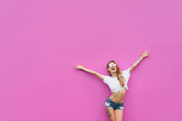 Young excited sporty woman with rised hands against pink wall.