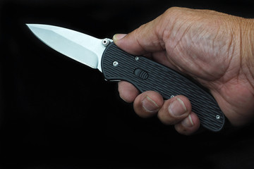 folding knife in hand on dark background.