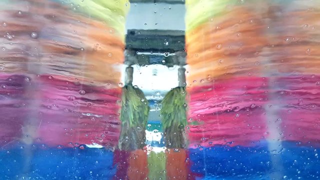 Rotating brushes and running water with soap in a car wash, view from inside through the windscreen.