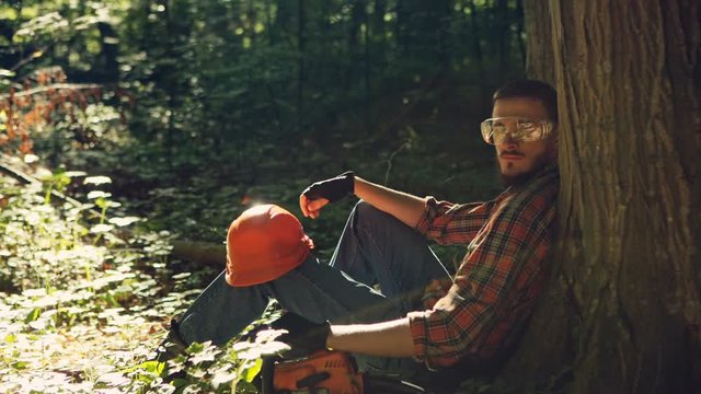 Male logger sitting on ground taking a break. RAW video record.