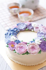 Gorgeous cake covered in roses made of butter cream icing on white wooden background