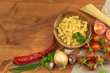 Raw pasta with tomatoes and parsley on a wooden background. Preparation diet food. The recipe for a simple dinner. Traditional pasta with vegetables.
