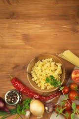 Raw pasta with tomatoes and parsley on a wooden background. Preparation diet food. The recipe for a simple dinner. Traditional pasta with vegetables.
