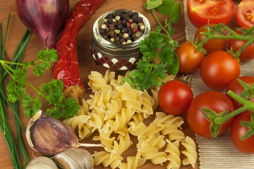 Raw pasta with tomatoes and parsley on a wooden background. Preparation diet food. The recipe for a simple dinner. Traditional pasta with vegetables.
