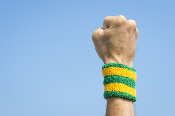 Close-up of Brazilian athlete wearing Brazil colors wristband punching the air against a bright blue sky