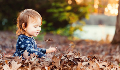 Happy toddler girl playing outside in a pile of leaves