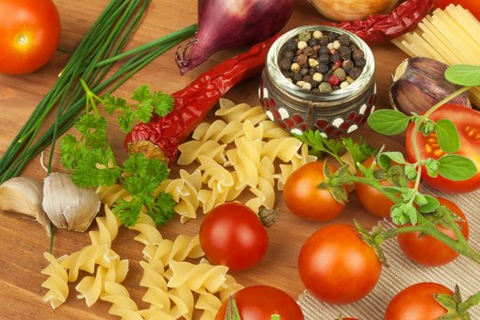 Raw pasta with tomatoes and parsley on a wooden background. Preparation diet food. The recipe for a simple dinner. Traditional pasta with vegetables.
