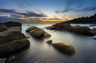 seascape with smooth wave, rock and sunset