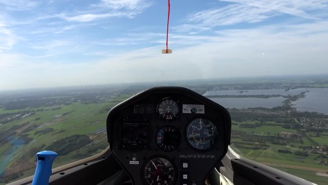 Cockpit point of view POV footage in modern glider sailplane flying towards lake showing advanced instrument panel with gauges reading altitude airspeed ascending speed beautiful day blue sky 4k