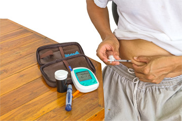 Male diabetes patient gets an insulin injection in abdomen area and equipment of blood glucose meter test kit on table over white background.