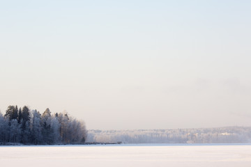 A beautiful winter landscape from Finland. Image taken during cold winter day on the lake ice. Some clouds are in the sky. Snow is covering the ice and lakeside. 