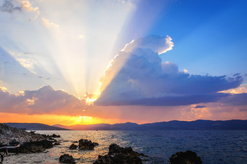 Sun beams or light rays breaking through the clouds at sunset, over the sea