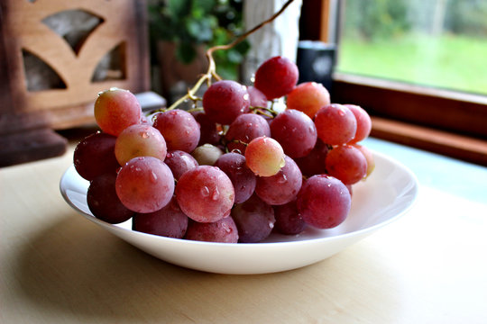 bunch of red grape with water drops on a white plate