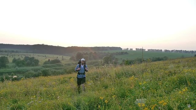 A bearded man with a backpack walking in the field. Sunset. Summer