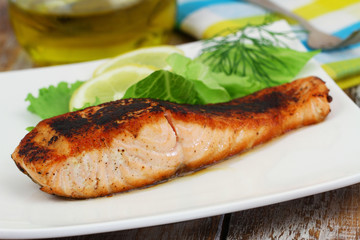 Grilled salmon steak with green salad and lemon on white plate
