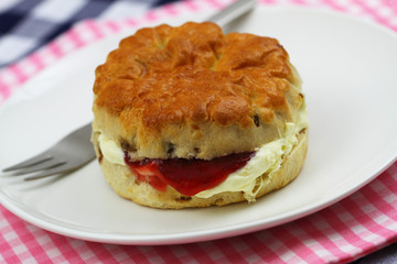 Home made English scone with traditional clotted cream and strawberry jam on white plate, closeup
