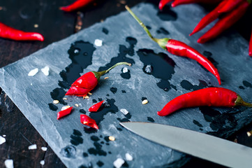 Slicing Chilli pepper with Knife on kitchen board