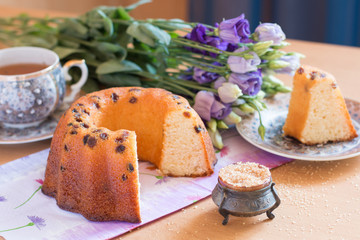 Cake with raisins, a cup of tea, bouquet of lilac flowers and a little vintage sugar-bowl with brown sugar on the foreground