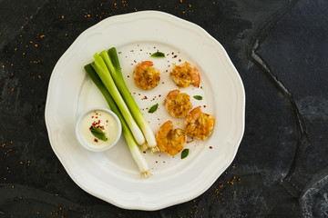 Grilled shrimp served on a white plate with fresh and crispy green onion.