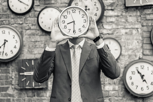 Man in suit standing near wall with clocks - Powered by Adobe