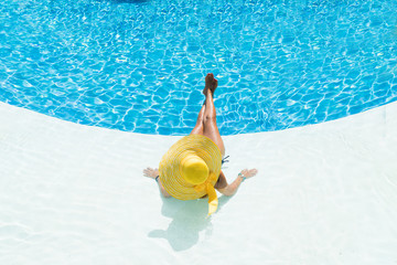 beautiful woman in a hat sitting on the edge of the pool