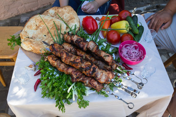 skewers of meat on a table in a garden with tomatoes, tortillas and vegetables