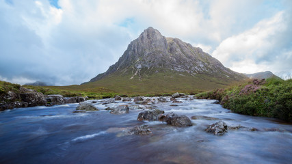 Beautiful river with rocks in it flowing in a scottish Valley next to a huge mountain in the background. 