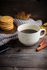 Cup of coffee/tea, cookies, fallen leaves, earphones, and scarf on wooden table.