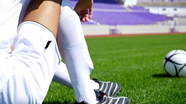 Footballer in white outfit adjusting his socks on the field