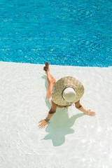 beautiful woman in a hat sitting on the edge of the pool