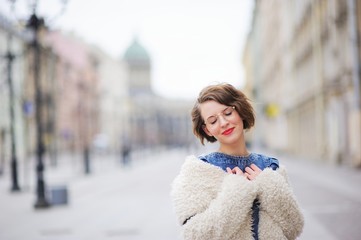Beautiful young smiling girl posing on the boulevard in the center of St. Petersburg, closing her...