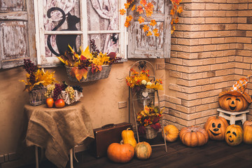 Old house patio in autumn season: shutters entwined with yellow leaves, halloween pumpkins lying on...