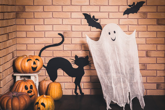 Funny Halloween decoration with smiling ghost and pumpkins, black painted bats and cat on the brick wall background