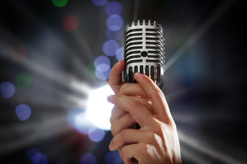 Female hands with vintage microphone on blurred lights background