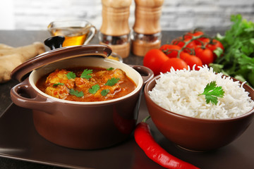Tasty dinner with chicken curry in saucepan and rice in bowl
