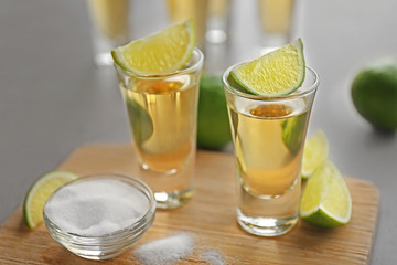 Shots of gold tequila with lime slices and salt on wooden board